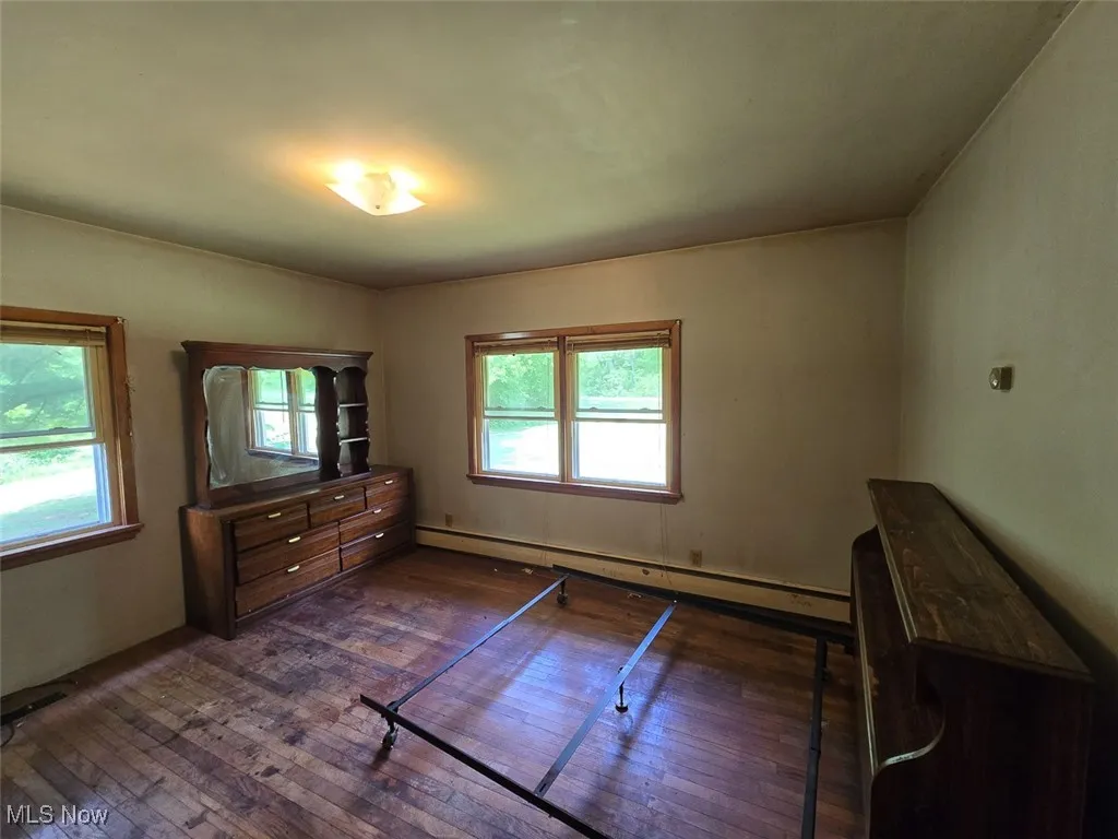 Unfurnished bedroom with dark wood finished floors and a baseboard heating unit