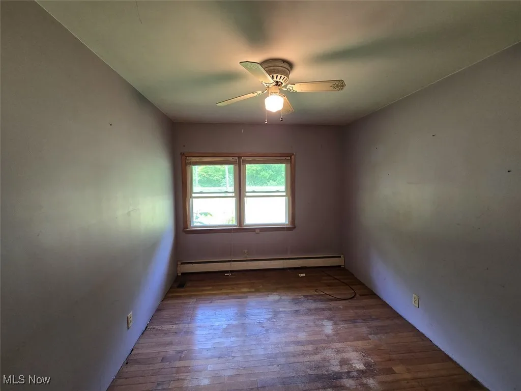 Unfurnished room featuring wood finished floors, a baseboard radiator, and ceiling fan