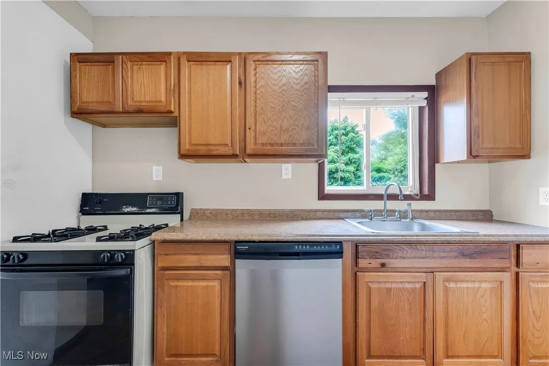 Kitchen with gas range, dishwasher, light countertops, and brown cabinets