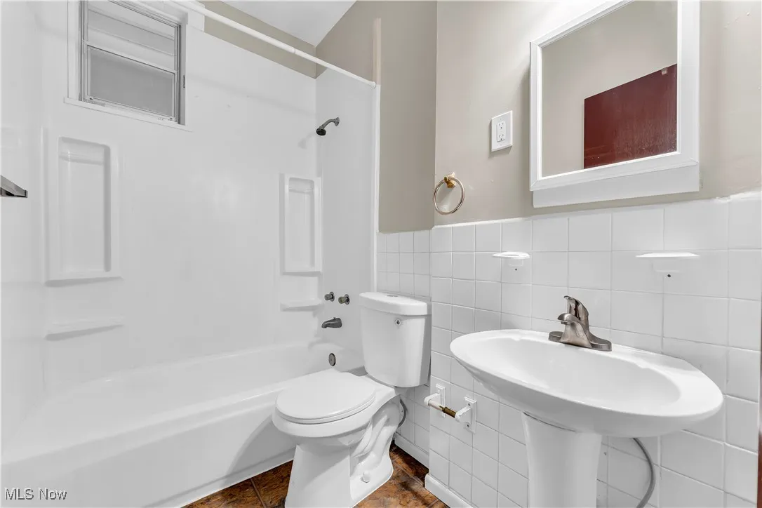 Full bath featuring  shower combination, tile walls, and a wainscoted wall