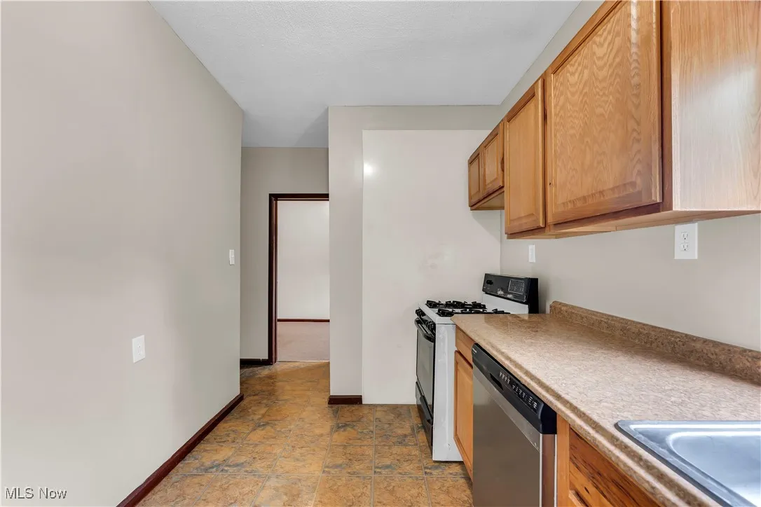 Kitchen with gas stove, stainless steel dishwasher, light countertops, and stone finish flooring