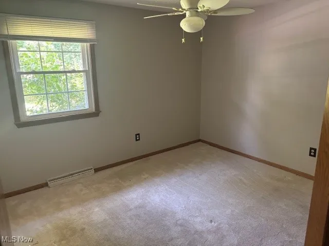Empty room with ceiling fan and light colored carpet
