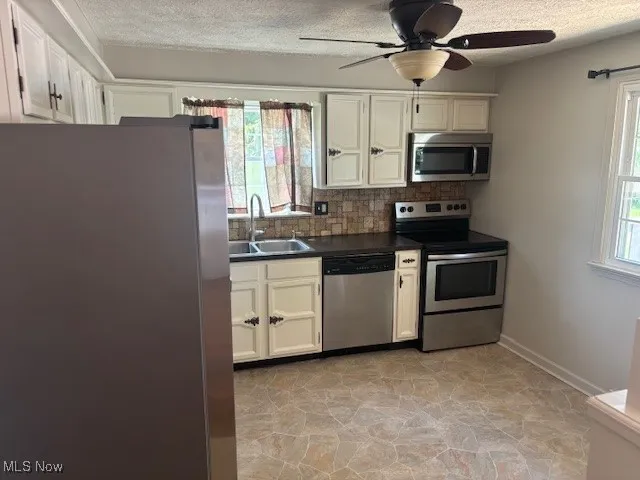 Kitchen featuring appliances with stainless steel finishes, dark countertops, a textured ceiling, decorative backsplash, and a ceiling fan
