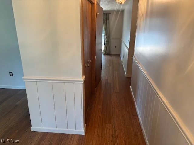Hallway featuring a decorative wall, a wainscoted wall, and dark wood finished floors