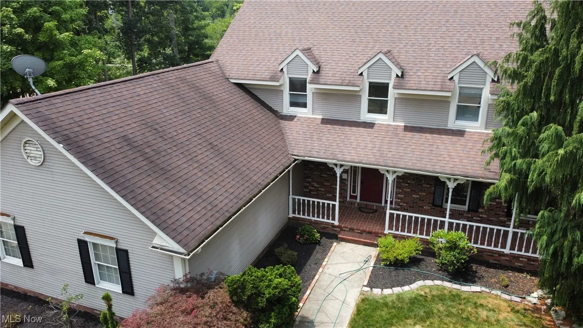 View of front of home featuring a shingled roof, brick siding, and covered porch