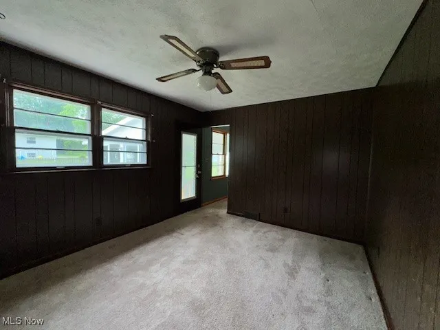 Empty room featuring wood walls, ceiling fan, and light colored carpet