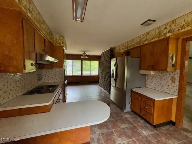 Kitchen with brown cabinets, stainless steel fridge with ice dispenser, decorative backsplash, light countertops, and a ceiling fan