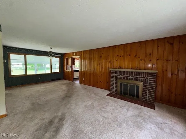 Unfurnished living room with plenty of natural light, a fireplace, wooden walls, and carpet