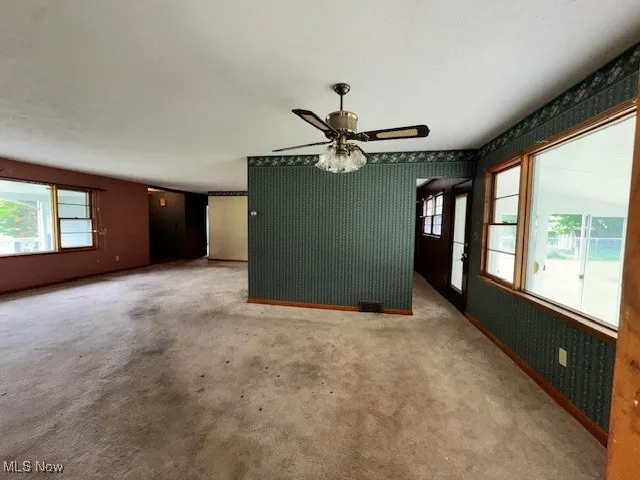 Unfurnished living room with ceiling fan, wallpapered walls, and carpet floors