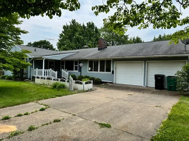Ranch-style house with an attached garage, concrete driveway, a front yard, a chimney, and covered porch