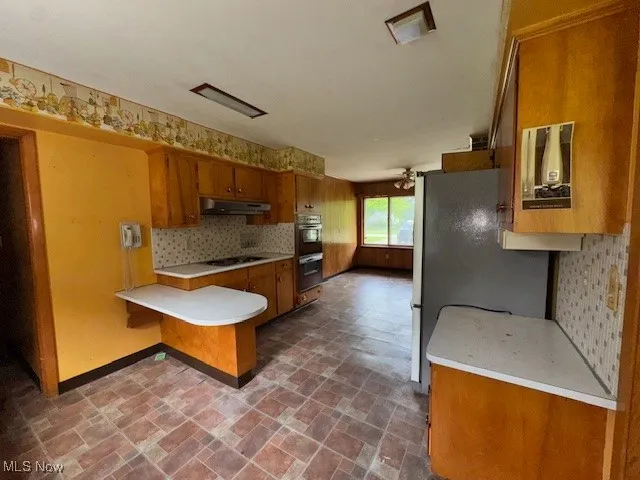 Kitchen with brown cabinets, a peninsula, light countertops, and appliances with stainless steel finishes