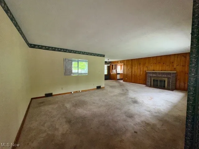 Unfurnished living room featuring a brick fireplace, carpet, and wood walls