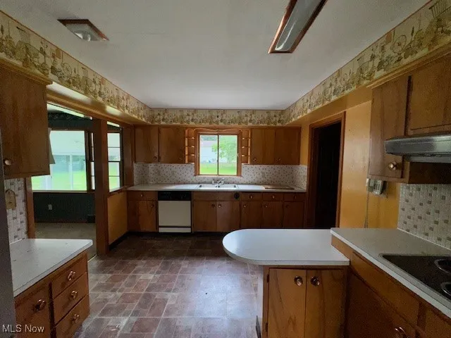 Kitchen featuring brown cabinetry, light countertops, backsplash, and dishwasher