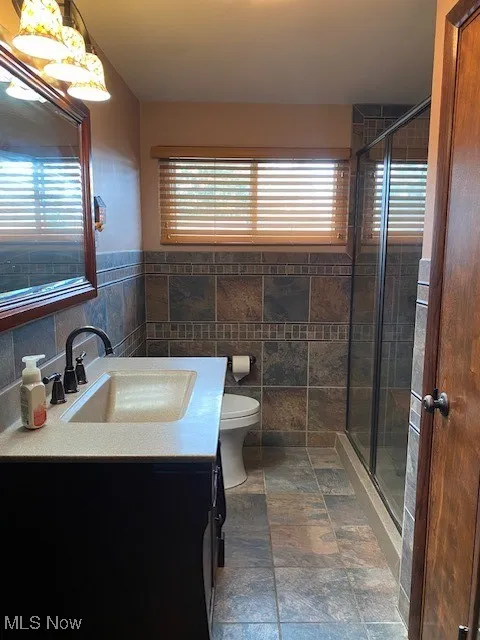 Bathroom featuring healthy amount of natural light, vanity, tile walls, a stall shower, and a wainscoted wall