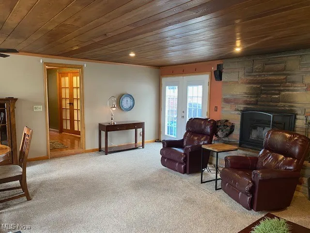 Carpeted living room featuring wood ceiling, french doors, crown molding, and a stone fireplace