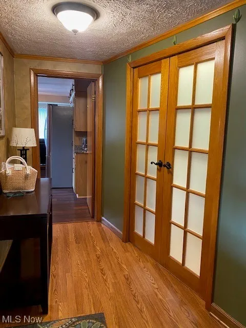 Hallway featuring french doors, wood finished floors, ornamental molding, and a textured ceiling