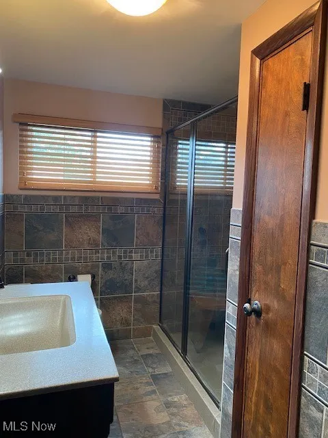 Full bathroom with a stall shower, vanity, tile walls, and stone finish flooring