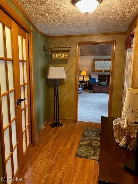 Hall featuring ornamental molding, wood finished floors, french doors, and a textured ceiling