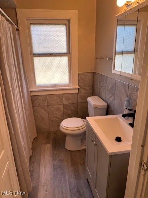 Full bath featuring tile walls, wood finished floors, vanity, a wainscoted wall, and a shower with curtain