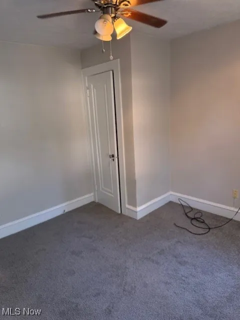 Carpeted spare room with a ceiling fan and baseboards