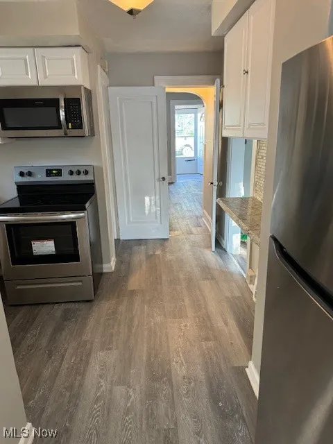 Kitchen featuring stove, fridge, white cabinetry, and dark wood finished floors