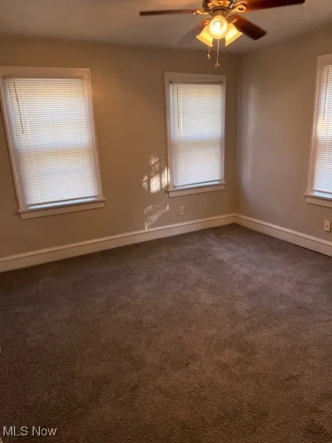 Spare room with a ceiling fan and dark colored carpet