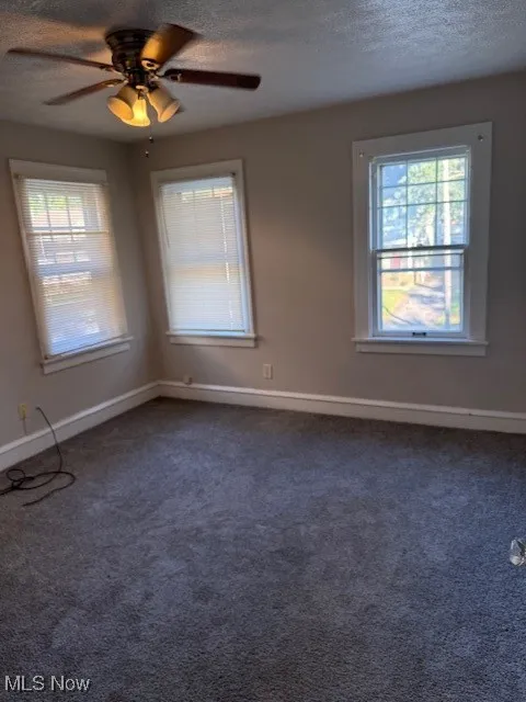 Unfurnished room with plenty of natural light, a textured ceiling, a ceiling fan, and dark colored carpet