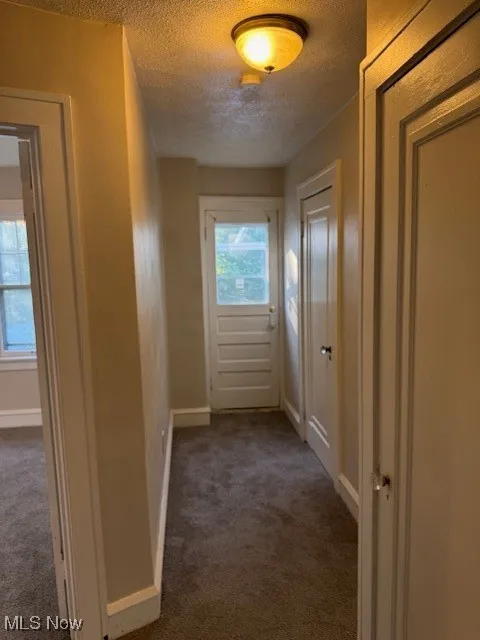 Hallway featuring dark carpet and a textured ceiling