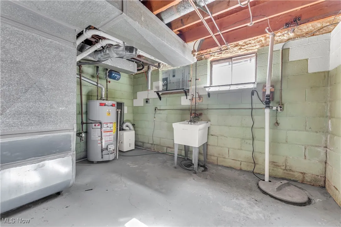 Basement featuring water heater, concrete block wall, and drainage system