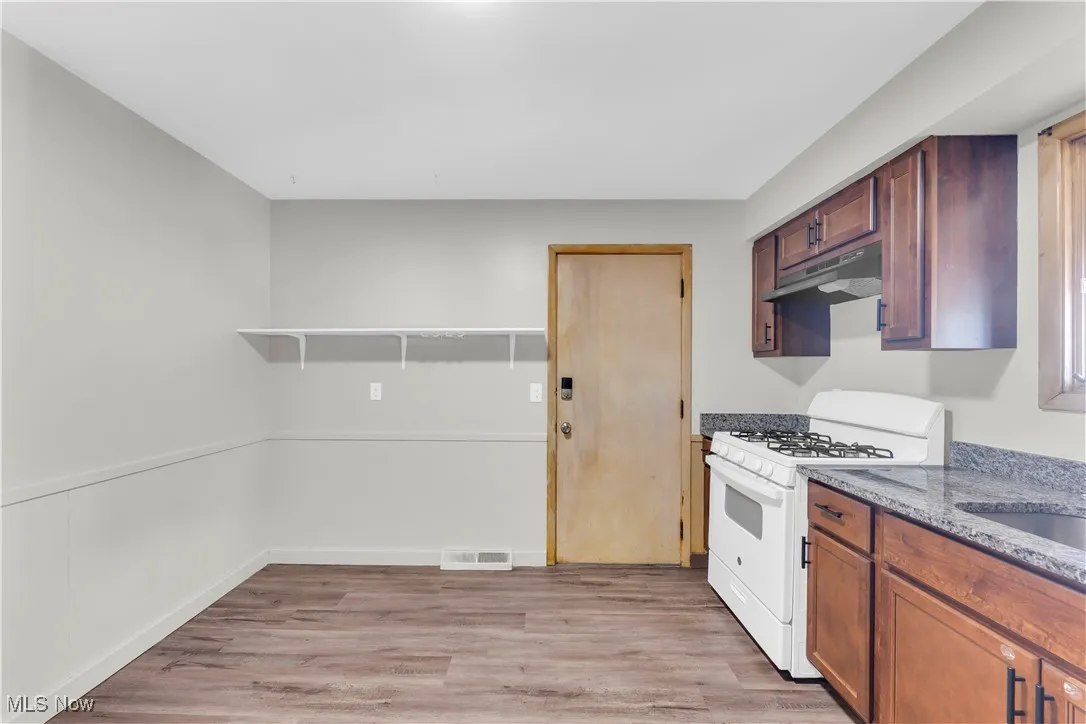 Kitchen with white gas range, light wood-type flooring, under cabinet range hood, open shelves, and light stone countertops