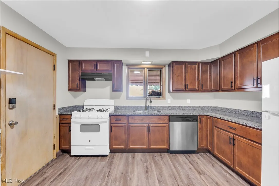 Kitchen with white appliances, light wood-type flooring, stone countertops, and under cabinet range hood