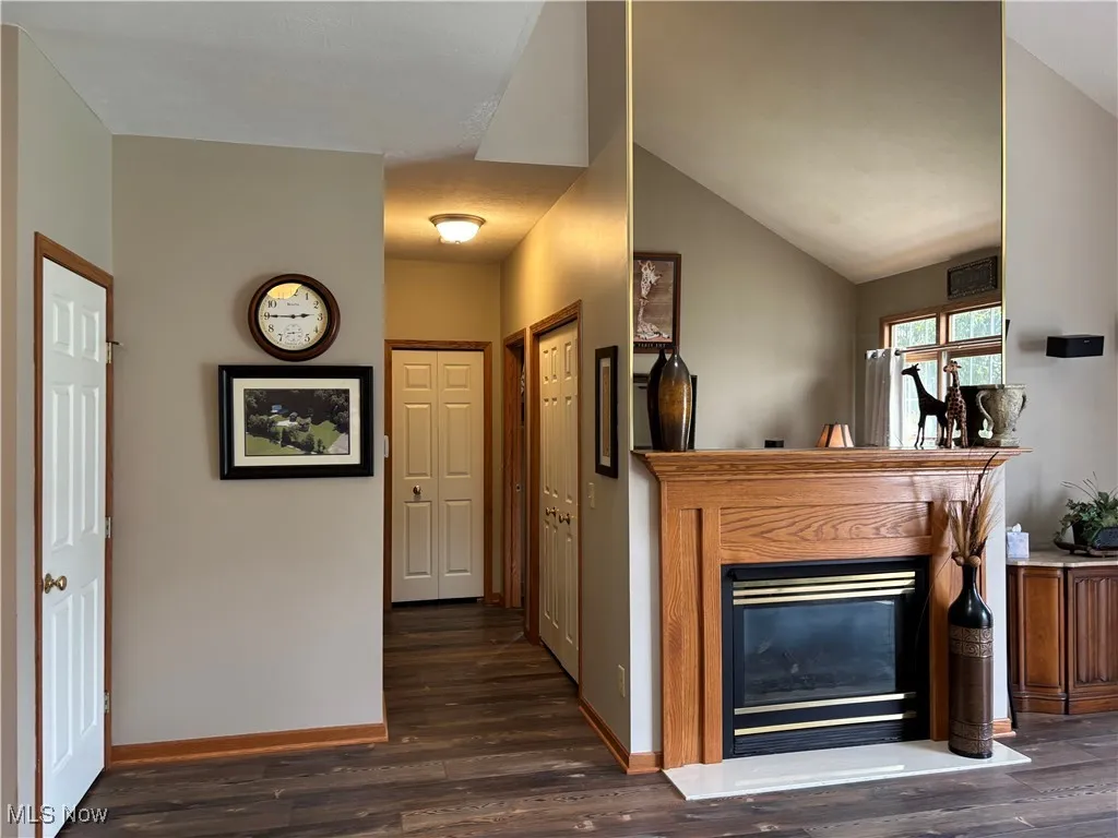 Living area featuring dark wood-style flooring, a glass covered fireplace, and lofted ceiling