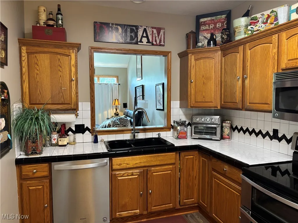 Kitchen with appliances with stainless steel finishes, decorative backsplash, brown cabinets, and tile countertops