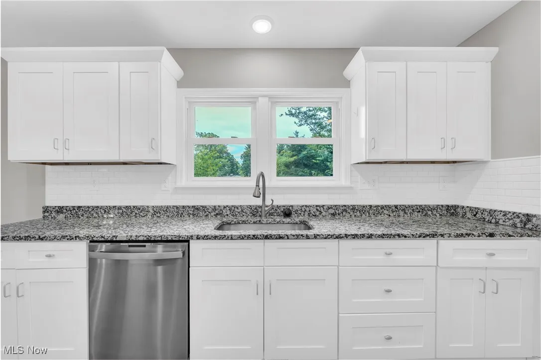 Kitchen featuring stainless steel dishwasher, dark stone countertops, white cabinetry, and decorative backsplash