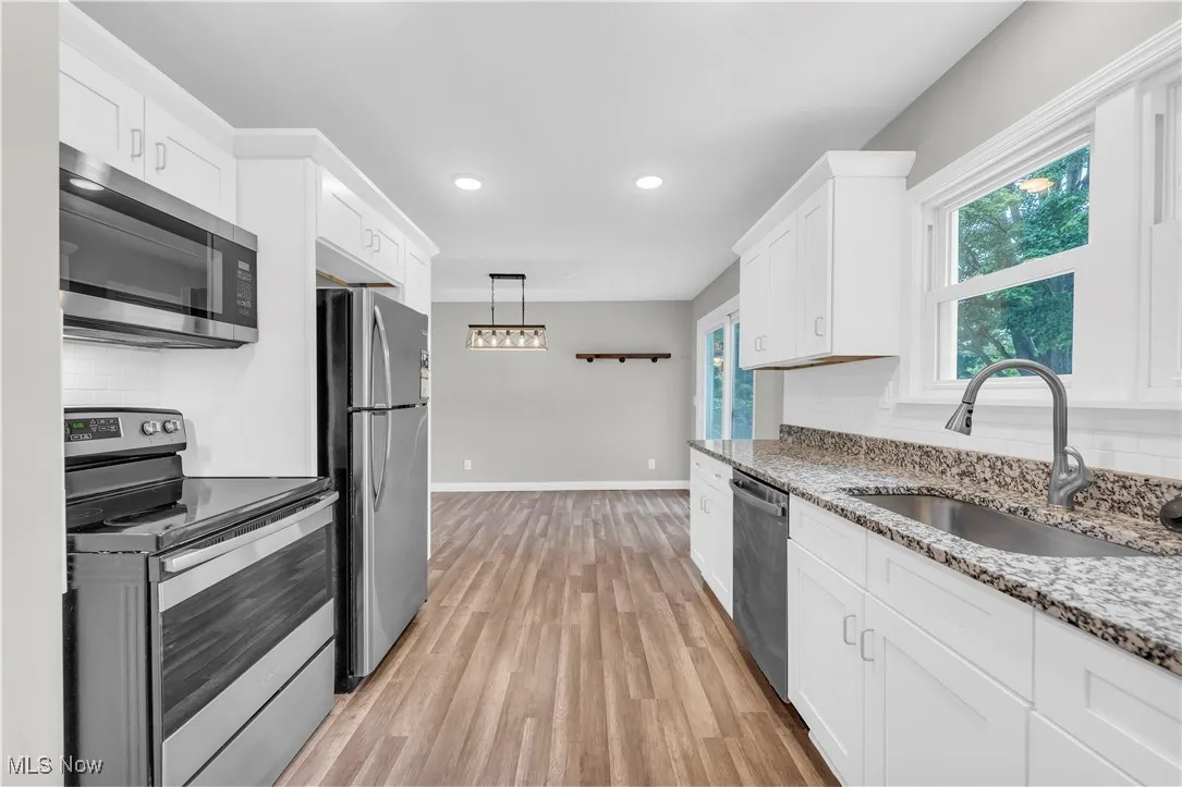 Kitchen featuring stainless steel appliances, white cabinets, light wood-style flooring, light stone countertops, and decorative backsplash
