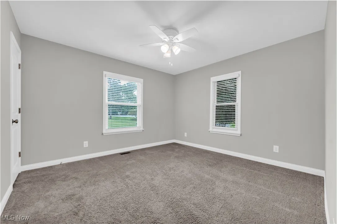 Carpeted empty room with a ceiling fan and baseboards