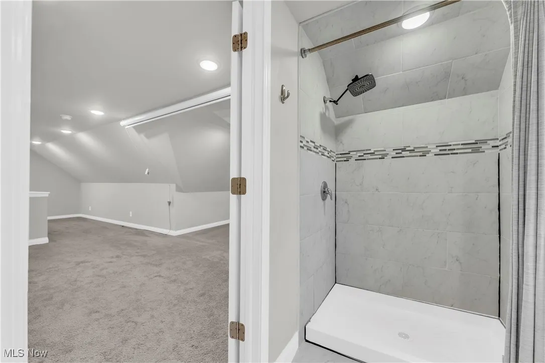 Full bathroom with a tile shower, vaulted ceiling, and recessed lighting