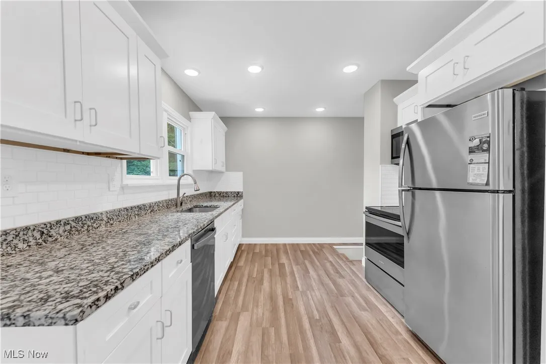Kitchen with stainless steel appliances, white cabinetry, tasteful backsplash, light wood finished floors, and stone countertops