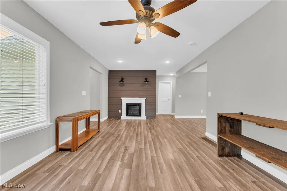 Unfurnished living room featuring light wood-type flooring, a glass covered fireplace, a ceiling fan, and recessed lighting