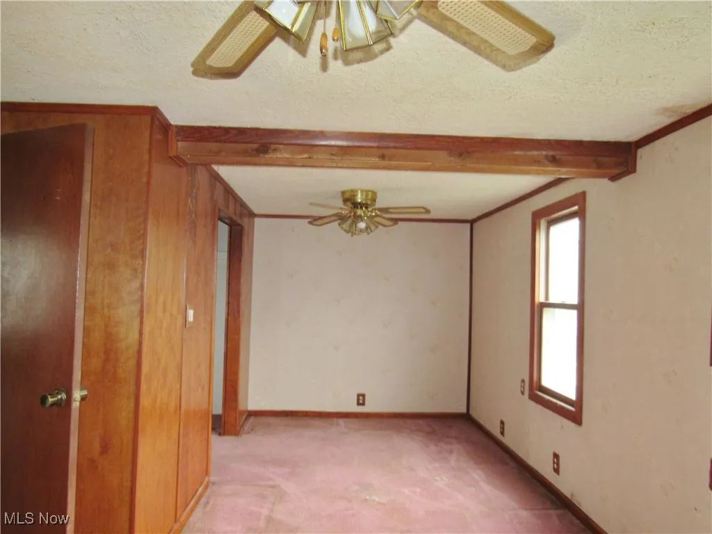 Unfurnished room featuring a ceiling fan, a textured ceiling, beam ceiling, and light carpet