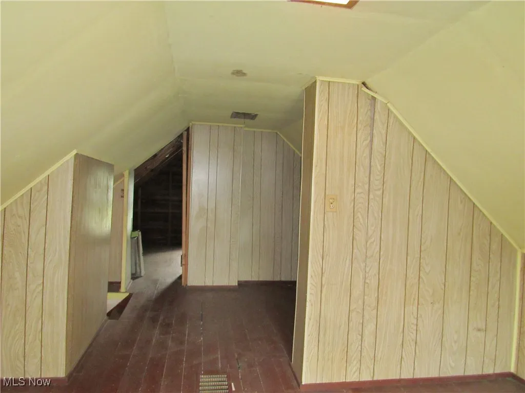 Bonus room with wood-type flooring, vaulted ceiling, and wooden walls