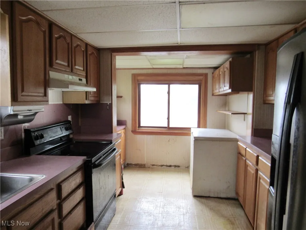 Kitchen with black appliances, under cabinet range hood, a paneled ceiling, dark countertops, and light flooring