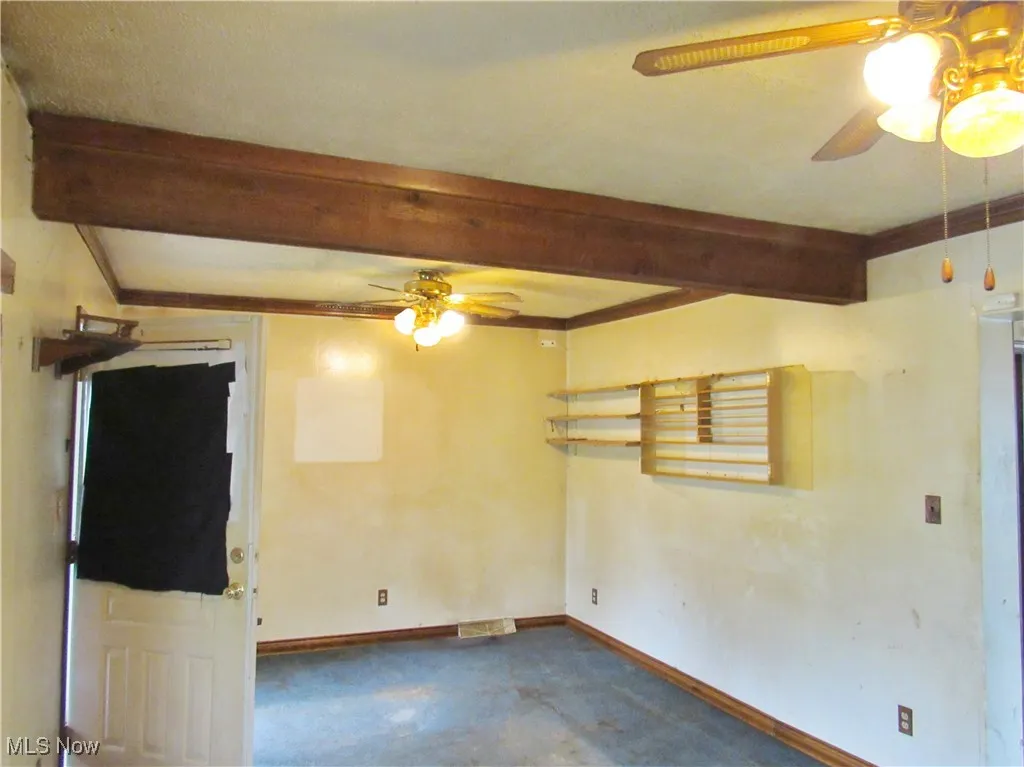 Empty room featuring ceiling fan and beam ceiling