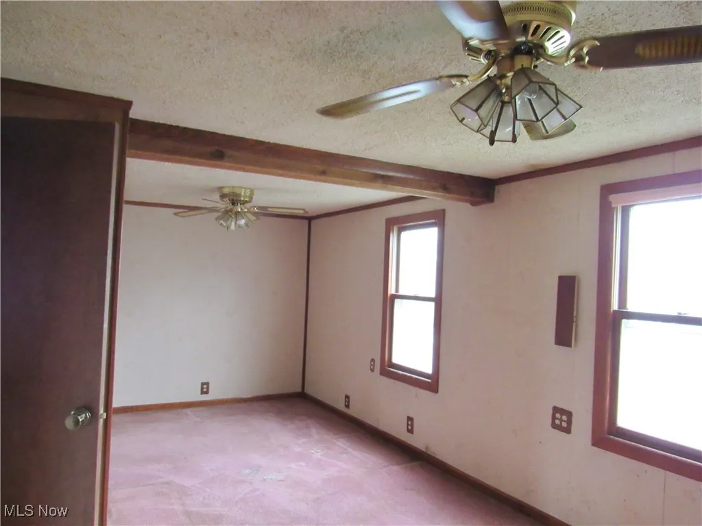 Unfurnished room featuring a textured ceiling, beamed ceiling, a ceiling fan, and light carpet