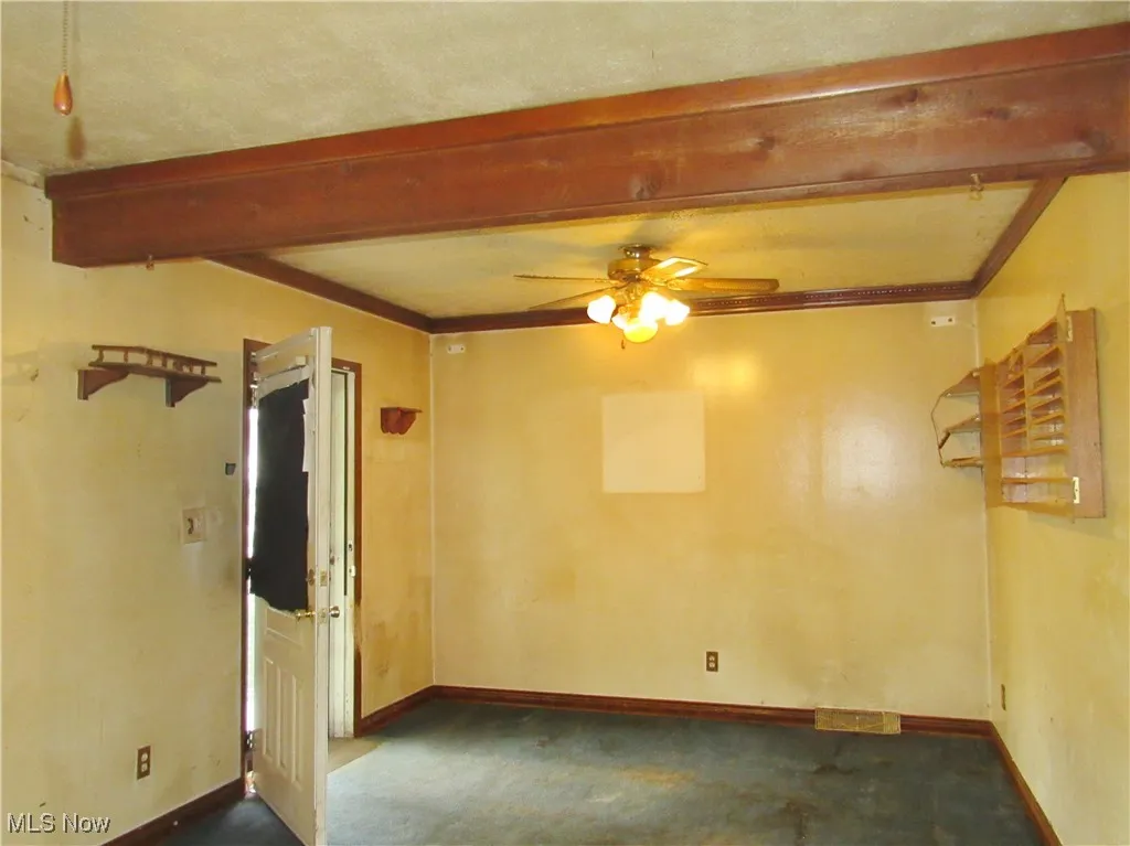 Spare room featuring beam ceiling, carpet flooring, a ceiling fan, and crown molding