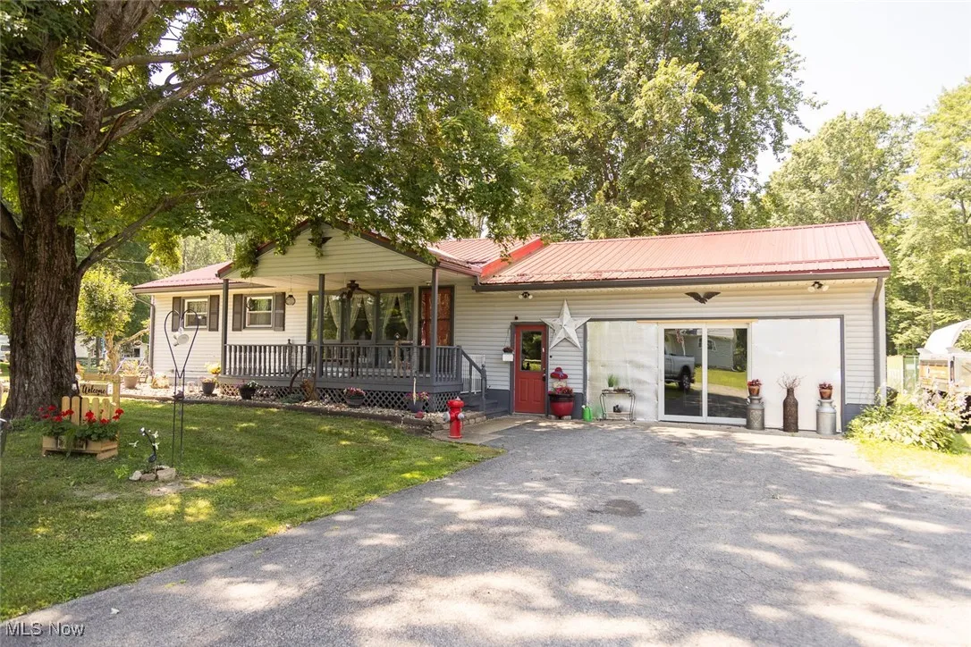 Ranch-style house featuring covered porch, driveway, a front yard, and a metal roof