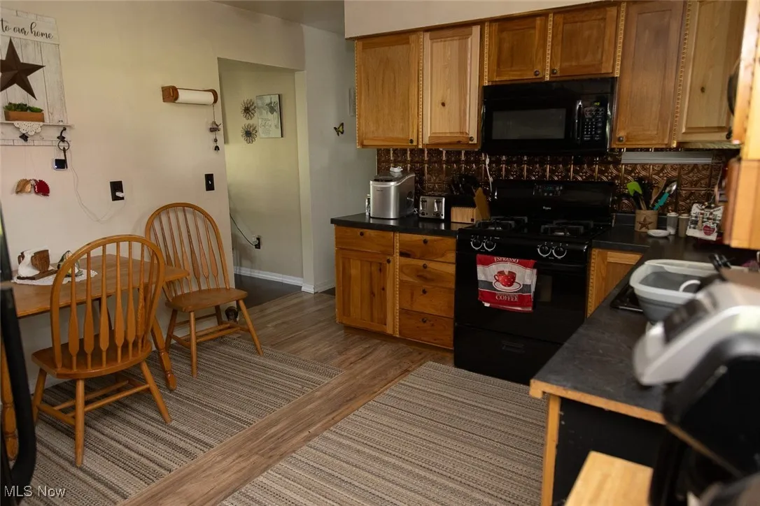 Kitchen featuring black appliances, backsplash, dark countertops, and wood finished floors