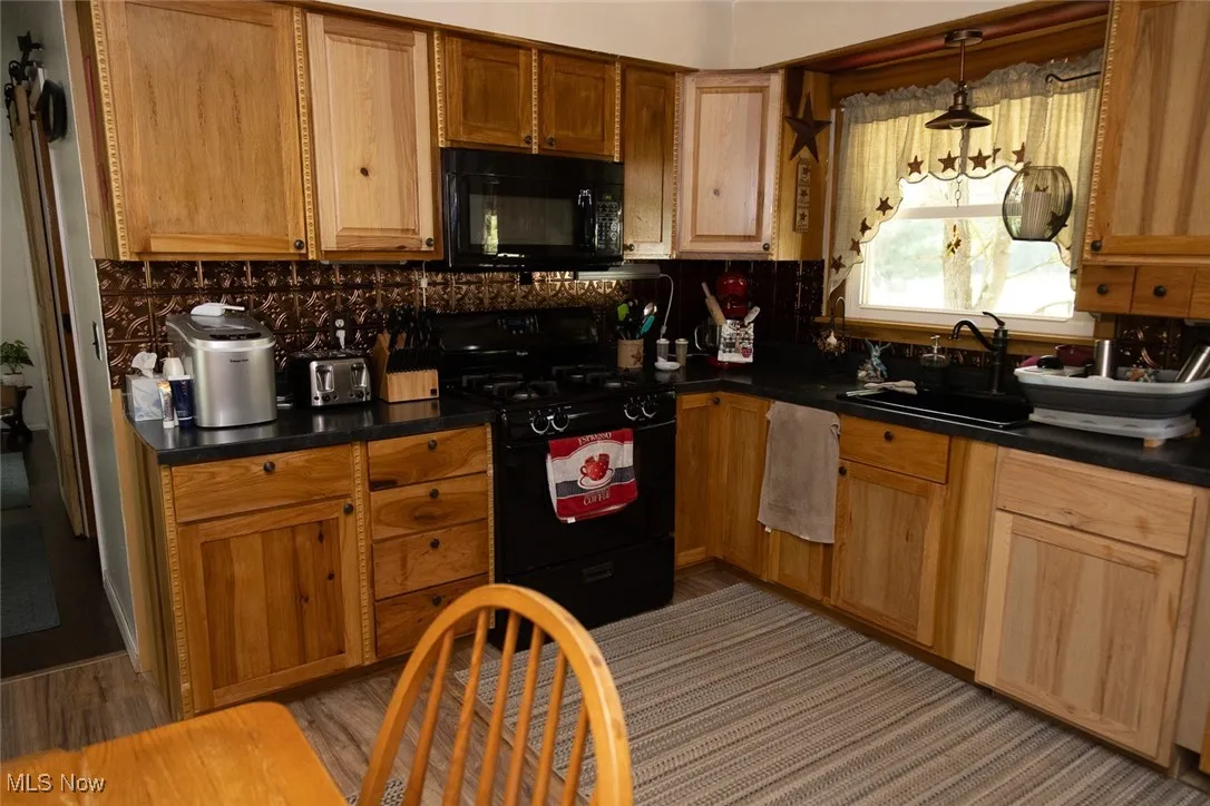 Kitchen with black appliances, backsplash, dark countertops, and hanging light fixtures