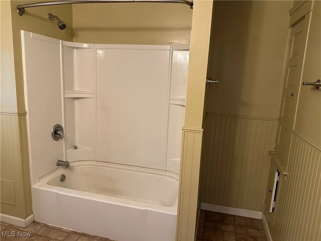Full bath with a wainscoted wall, shower / bath combination, and stone finish floors