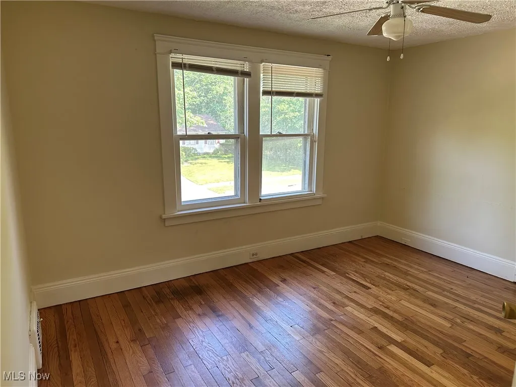 Empty room with a ceiling fan, hardwood / wood-style flooring, and a textured ceiling